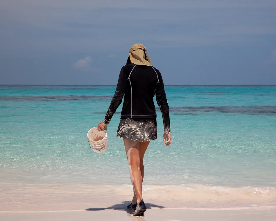 Someone walking the waterline with a bucket, the reef line dark behind the turquoise shallows