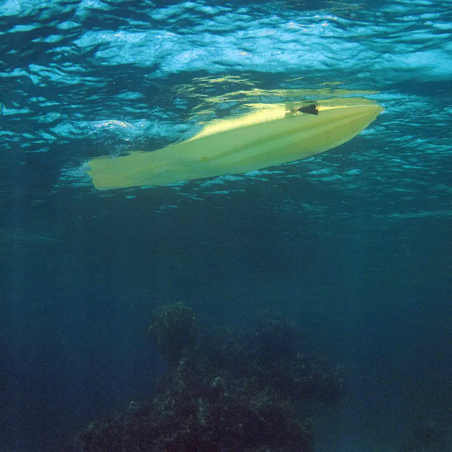The yellow hull of a kayak seen from underwater, floating on the rippled surface with the reef below