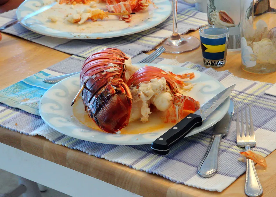 Two grilled Bahamian lobster tails on a plate, split and dressed, on a striped placemat