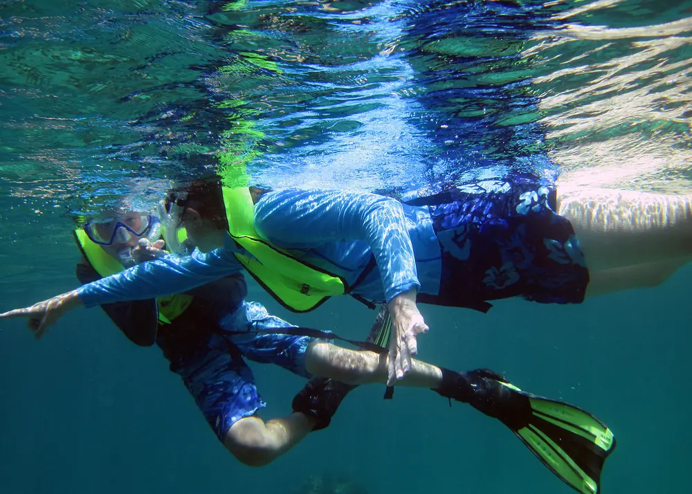 Two snorkellers at the surface seen from below, fins and masks against the light on the water