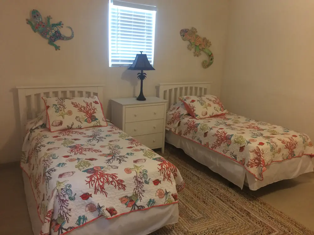 The twin room: two single beds under painted geckos, made up in coral reef quilts, with a woven rug between them